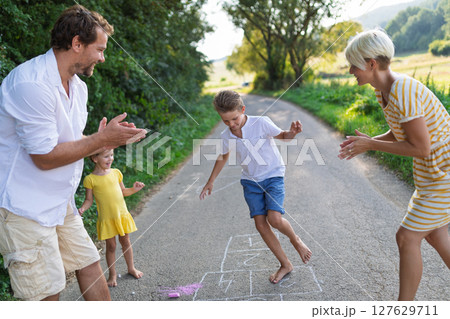 A young family with small children playing hopscotch on a road in summer. 127629711