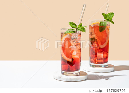 Two glasses of cocktail with grapefruit, mint and ice on marble stand on a white yellow background Two glasses of cocktail with grapefruit, mint and ice on marble stand on a white yellow background 127629793