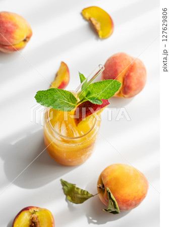 Peach drink or tea with ice, mint in a glass on a white table with fresh fruits and sunlight. Peach drink or tea with ice, mint in a glass on a white table with fresh fruits and sunlight. 127629806