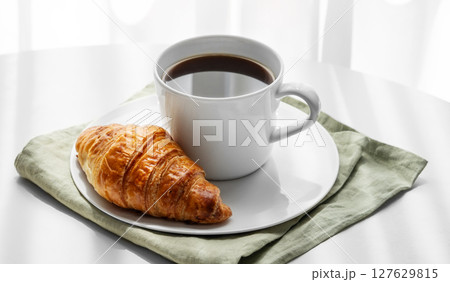 Cup of espresso coffee and fresh croissant on napkin on white table near window 127629815