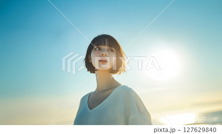 夕焼けの中、防波堤に立つ女性 127629840