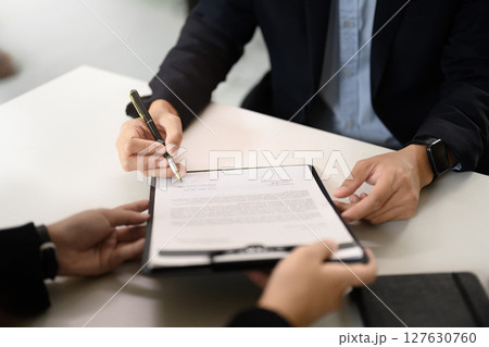 Close up of two business professionals reviewing and signing a contract at office desk Close up of two business professionals reviewing and signing a contract at office desk 127630760