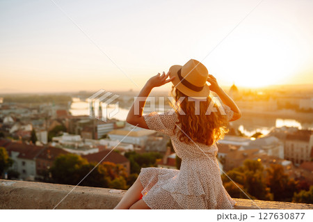 Portrait of happy woman tourist in hat at dawn enjoys cityscape. concept of an active lifestyle. 127630877