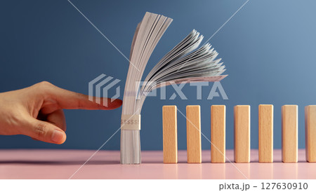 A finger about to push US dollar stack onto dominos, symbolizing economic risk, global financial instability, and the impact of powerful nations like the USA 127630910