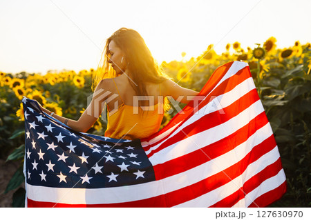 Woman proudly hold waving american USA flag in in the sunflower field. Independence Day, 4th July. 127630970