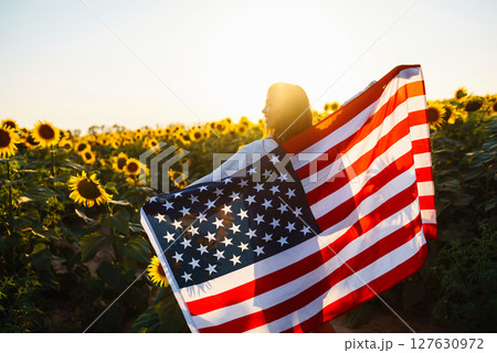 Woman proudly hold waving american USA flag in in the sunflower field. Independence Day, 4th July. Woman proudly hold waving american USA flag in in the sunflower field. Independence Day, 4th July. 127630972