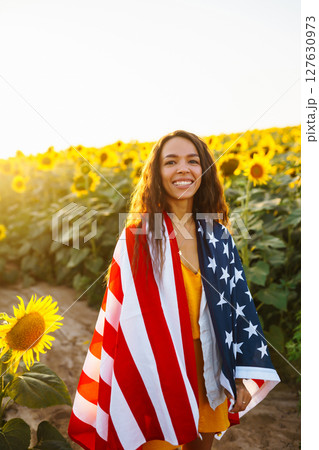 Woman proudly hold waving american USA flag in in the sunflower field. Independence Day, 4th July. Woman proudly hold waving american USA flag in in the sunflower field. Independence Day, 4th July. 127630973