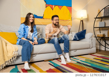 Man and woman in casual clothes watching match on TV at home cheering with excitement Man and woman in casual clothes watching match on TV at home cheering with excitement 127631017