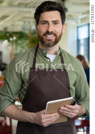 Young bearded man in apron looking confident while waiting for the client in pizzeria 127631092