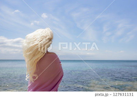 Blonde hair beach: Woman stands, enjoys summer breeze on sunny seaside, showing carefree vacation freedom. 127631131