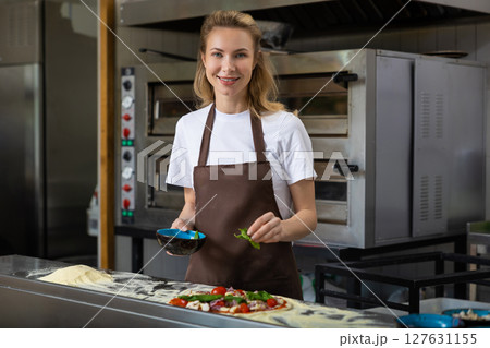 Smiling young female cooker looking happy in the pizzeria kitchen 127631155