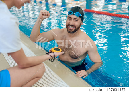 Man having a workout in the swimming pool and talking with his coach 127631171