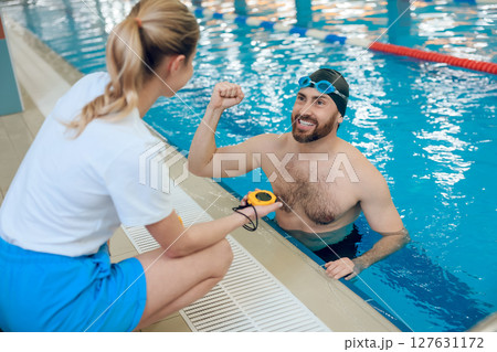 Man having a workout in the swimming pool and talking with his coach Man having a workout in the swimming pool and talking with his coach 127631172