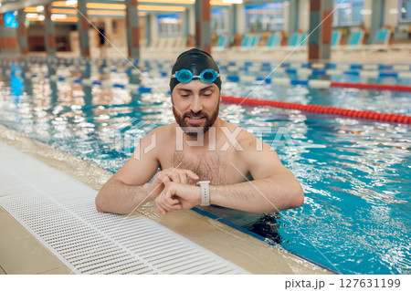 Man having a workout in the swimming pool and looking at his watch 127631199