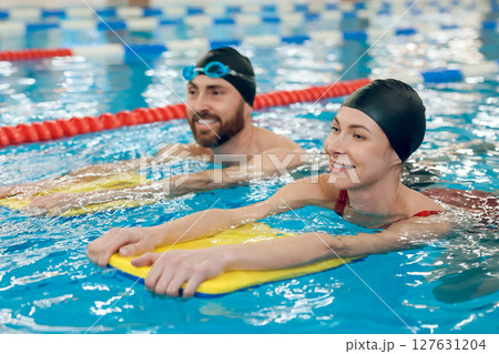 Young cute couple in swimming with boards in the pool Young cute couple in swimming with boards in the pool 127631204