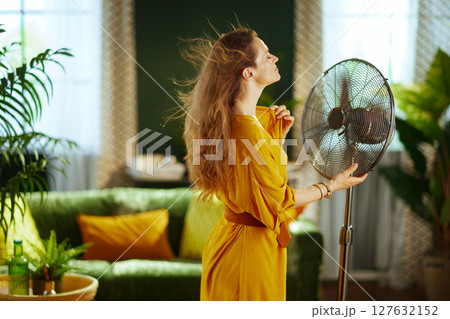 Modern Living Room, Woman Cooling Down with Fan 127632152