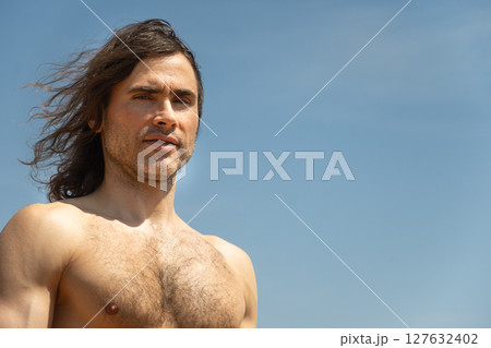 Shirtless sun-tanned happy young man with long hair against clear blue sky. Outdoors. Summer. Banner. 127632402