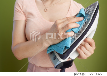 Close-up: Woman cleaning iron, peach shirt, pink skirt 127633278