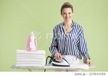Woman ironing clothes next to detergent and stack of towels 127633289