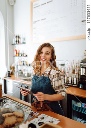 Successful small business owner stands behind counter of coffee shop with digital tablet takes order Successful small business owner stands behind counter of coffee shop with digital tablet takes order 127633433