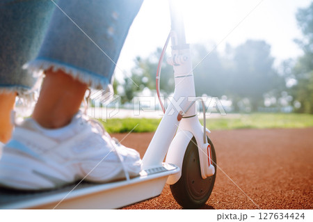 Woman riding electric kick scooter outdoors at sunset, closeup. Ecological transportation concept. 127634424
