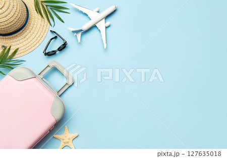 Pink suitcase, airplane model, sunglasses and straw hat on blue background with copy space 127635018
