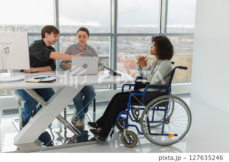 Teamwork brainstorm. Diverse multiracial colleagues woman in chair for people with disability working together. Group of people sitting in creative office discussing business. Young professional team Teamwork brainstorm. Diverse multiracial colleagues woman in chair for people with disability working together. Group of people sitting in creative office discussing business. Young professional team 127635246