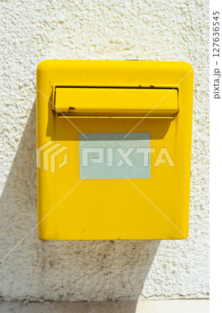 Yellow mailbox on bright white wall. Postal service, communication symbol, and street detail in sunny environment. 127636545
