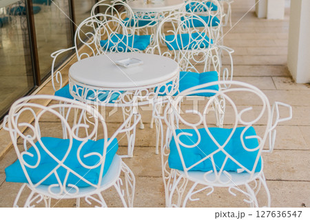 White patio chairs with blue cushions in sunny veranda close-up. Outdoor elegance, Mediterranean leisure, and summer hospitality design. 127636547