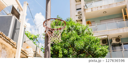 Old basketball hoop in urban courtyard under the summer sky, banner with copy space. Concept of street sports, childhood memories, and outdoor recreation in residential neighborhoods. Old basketball hoop in urban courtyard under the summer sky, banner with copy space. Concept of street sports, childhood memories, and outdoor recreation in residential neighborhoods. 127636596