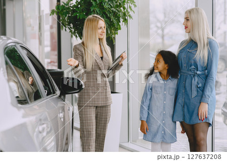 Family in a car salon. Woman buying the car. Little african girl with mther. Manager with clients. 127637208