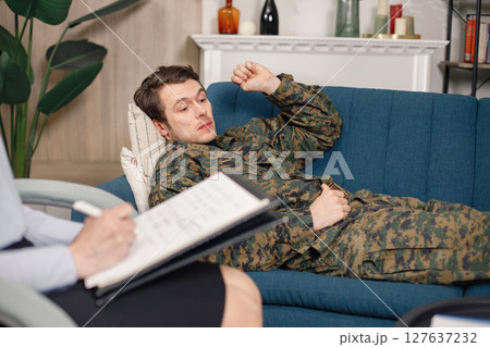 Cropped photo of soldier laying on couch during therapy session. Man wearing military uniform. Male warrior with ptds talking to psychiatrist. 127637232