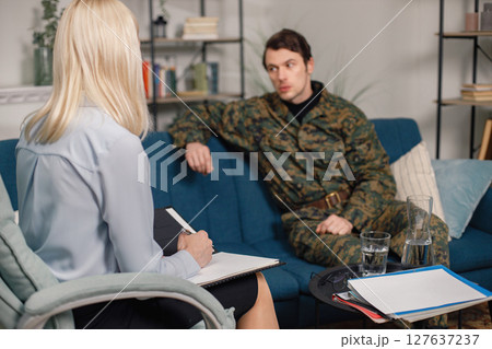 Soldier and psychiatrist sitting on couch during therapy session. Man wearing military uniform. Male warrior with ptds talking to psychiatrist. Soldier and psychiatrist sitting on couch during therapy session. Man wearing military uniform. Male warrior with ptds talking to psychiatrist. 127637237