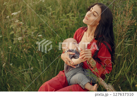 Mother with cute daughter. Mom breastfeeding her little son. Woman in a red dress. Mother with cute daughter. Mom breastfeeding her little son. Woman in a red dress. 127637310