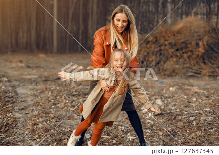 Fashionable mother with daughter. Family in a autumn park. Little daughter in a brown coat. 127637345