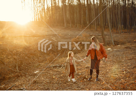 Fashionable mother with daughter. Family in a autumn park. Little daughter in a brown coat. 127637355