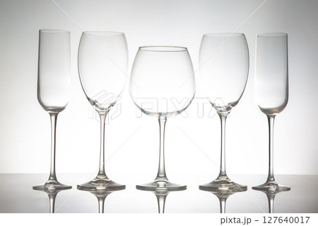 A sleek lineup of five elegant, empty wine glasses with long stems, reflecting on a glossy surface A sleek lineup of five elegant, empty wine glasses with long stems, reflecting on a glossy surface 127640017