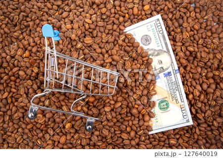 Mini shopping cart on roasted coffee beans with US dollar bills, symbolizing coffee trade Mini shopping cart on roasted coffee beans with US dollar bills, symbolizing coffee trade 127640019