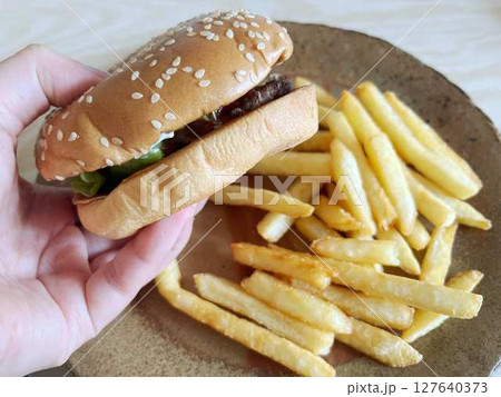 ハンバーガーとフライドポテトを食べる手 127640373