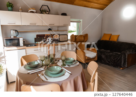 Cozy Cabin Kitchen Dining Area Interior with Modern Appliances, Beige Decor, Warm Lighting, Comfortable Seating, Small Space Living, Rustic Style. Cozy Cabin Kitchen Dining Area Interior with Modern Appliances, Beige Decor, Warm Lighting, Comfortable Seating, Small Space Living, Rustic Style. 127640446