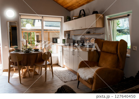 Cozy Cabin Interior with Rustic Wood Kitchen, Dining Area, Leather Armchair, and Natural Light Streaming Through Large Windows 127640450