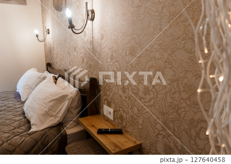 Cozy Bedroom Interior with Floral Wallpaper and Warm Lighting: A Relaxing Scene Featuring a Bedside Table, Sconces, and Decorative Lights Cozy Bedroom Interior with Floral Wallpaper and Warm Lighting: A Relaxing Scene Featuring a Bedside Table, Sconces, and Decorative Lights 127640458
