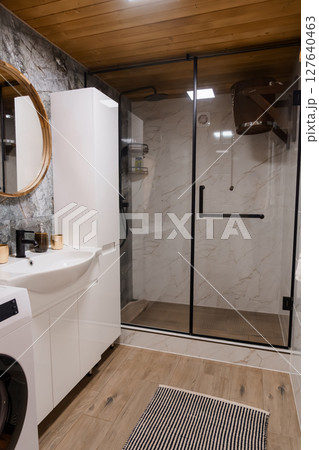 Modern Bathroom Design Featuring Walk-in Shower, White Vanity, Marble Tile and Wood Accents, Elegant Interior, Spa-like Ambiance, Neutral Color Palette. 127640463