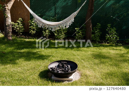Relaxing Backyard Oasis with White Hammock and Fire Pit. Cozy Outdoor Living Space, Lush Greenery, Warm Lighting, Peaceful Summer Scene 127640480