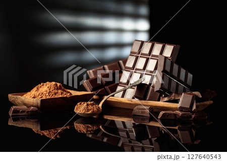 Broken bitter chocolate bars and wooden dish with cocoa powder. Broken bitter chocolate bars and wooden dish with cocoa powder. 127640543
