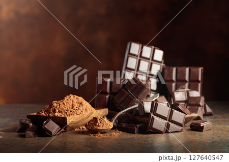 Scraps of dark chocolate next to a wooden bowl of cocoa powder. 127640547