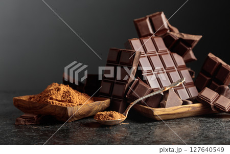 Broken dark chocolate bar and cocoa powder on a black background. 127640549