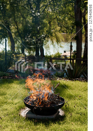 Backyard Fire Pit Scene: Warm Flames in Green Landscape, Lake View, Rustic Outdoor Living and Cozy Evening Ambiance with Smoldering Wood Backyard Fire Pit Scene: Warm Flames in Green Landscape, Lake View, Rustic Outdoor Living and Cozy Evening Ambiance with Smoldering Wood 127640698