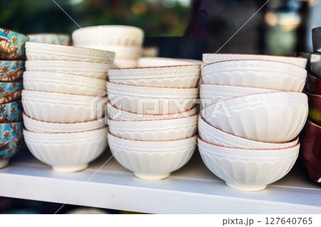 Stacked white ceramic bowls on store shelf. Kitchenware organization, ceramic tableware, and minimalist design in a retail display. Stacked white ceramic bowls on store shelf. Kitchenware organization, ceramic tableware, and minimalist design in a retail display. 127640765