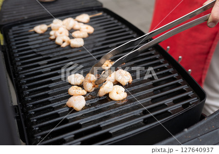 Caucasian adult grilling shrimp outdoors with metal tongs Caucasian adult grilling shrimp outdoors with metal tongs 127640937